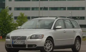 Srebrne Volvo V50 kombi zaparkowane przed nowoczesnym budynkiem.