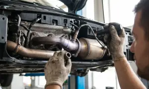 Mechanik w rękawiczkach naprawia katalizator p0420. Widać podniesiony samochód i elementy układu wydechowego.