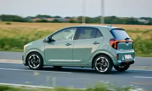 Zielony Kia Picanto w ruchu drogowym, widok z boku, z polem w tle.