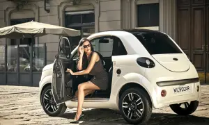 Elegancka kobieta w okularach przeciwsłonecznych wysiada z białego samochodu Microcar. Idealny samochód bez prawa jazdy na miejskie wypady.
