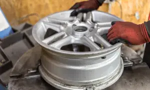 Ręce w rękawiczkach ustawiają aluminiową felgę na maszynie. Zastanawiasz się, ile kosztuje prostowanie felg?