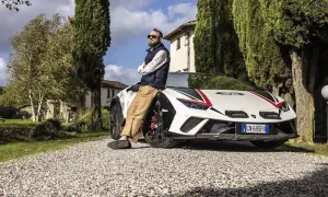 Mężczyzna opiera się o białe Lamborghini Sterrato z czerwono-czarnymi akcentami, zaparkowane na żwirowej drodze wśród drzew.