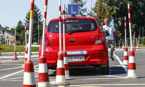 Czerwony Hyundai na placu manewrowym, gotowy do egzaminu na prawo jazdy B. Instruktor pokazuje znak zwycięstwa.