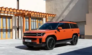 Pomarańczowy, luksusowy SUV Santa Fe stoi przed nowoczesnym budynkiem z drewnianą pergolą.