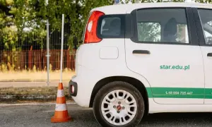 Szukasz informacji, ile kosztuje prawo jazdy AM? Na zdjęciu biały samochód szkoleniowy z numerem telefonu i adresem strony internetowej szkoły jazdy.