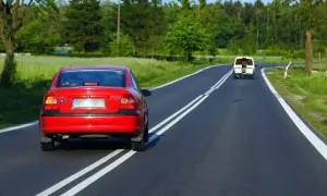 Czerwony Opel próbuje wyprzedzanie na podwójnej ciągłej, mandat murowany. Biały bus jedzie z przodu.
