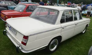 Białe BMW E10 z lat 70. prezentuje się elegancko na zielonej trawie, obok czerwonego klasyka.