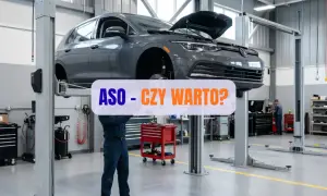 Szary samochód na podnośniku w ASO. Mechanik pracuje pod autem, a nad nim napis "ASO - CZY WARTO?".