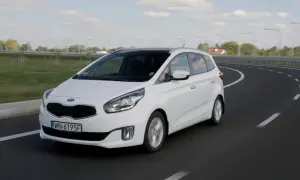 Biały Kia Carens 4 na zakręcie drogi.