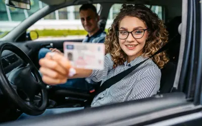 Szczęśliwa młoda kobieta z prawem jazdy w ręku, gotowa na swój okres próbny. Obok siedzi instruktor.
