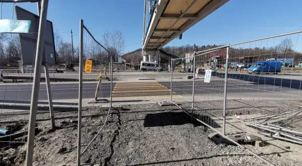 Przejście dla pieszych w budowie, ogrodzone siatką. W tle wiadukt i ruch uliczny. Kmy rejestracja.