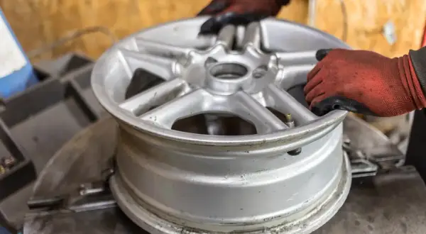 Ręce w rękawiczkach ustawiają aluminiową felgę na maszynie. Zastanawiasz się, ile kosztuje prostowanie felg?