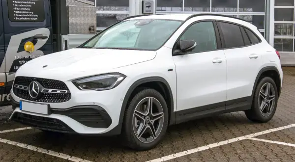 Biały Mercedes GLA, kompaktowy SUV, zaparkowany na mokrym parkingu. Jego wymiary idealnie pasują do miejskiej dżungli.