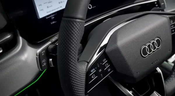 Wnętrze nowoczesnego samochodu Audi. Kierownica z przyciskami, ekran z informacjami o podróży i zielone podświetlenie. Czy to elektryczny samochód?