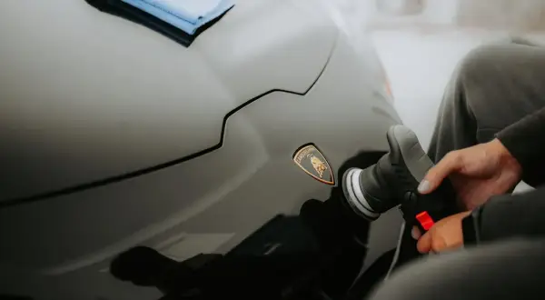 Ręka z polerką samochodową przy logo Lamborghini na czarnym lakierze.