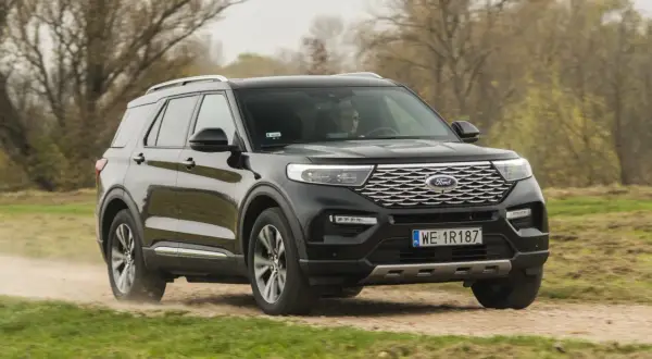 Czarny Ford Explorer 4x4 pokonuje piaszczystą drogę wśród jesiennej przyrody.