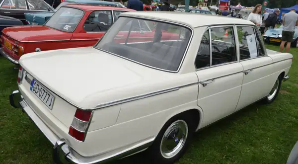 Białe BMW E10 z lat 70. prezentuje się elegancko na zielonej trawie, obok czerwonego klasyka.