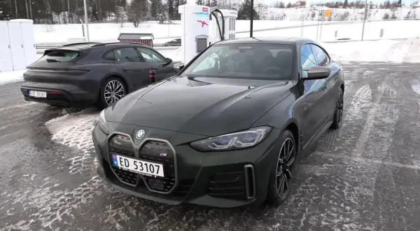 Zielone BMW i4 na ładowarce w zimowy dzień. Obok stoi ciemny Porsche Taycan.