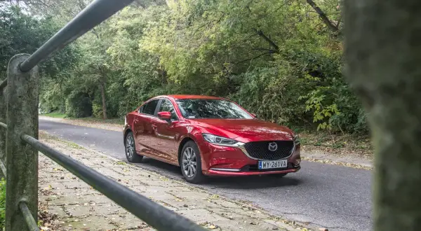 Czerwona Mazda 6 2.0 benzyna jedzie leśną drogą.