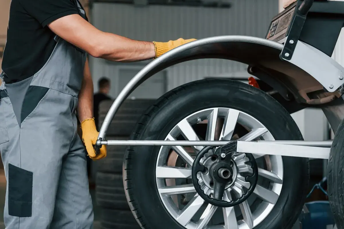 Mechanik w żółtych rękawiczkach sprawdza koło na wyważarce. Dowiedz się, ile kosztuje wymiana opon.