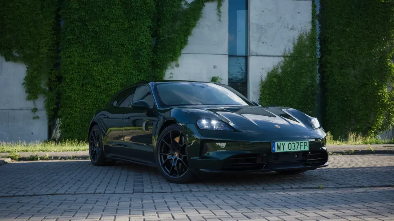 Ciemnozielony Porsche Taycan na tle nowoczesnego budynku z pnączami.