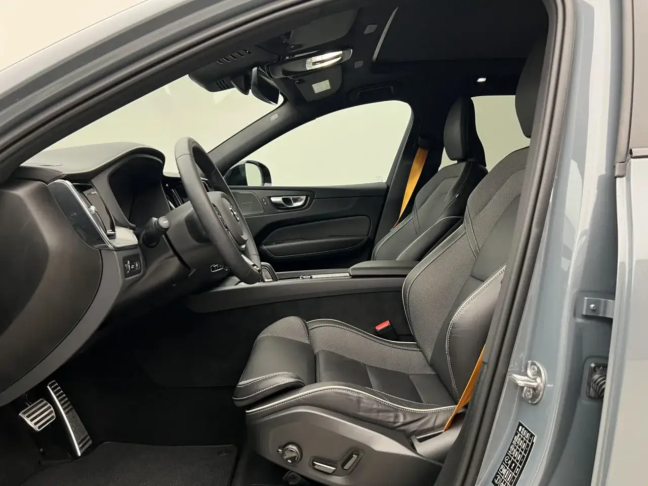 Wnętrze Volvo XC60 Polestar z czarnymi skórzanymi fotelami i żółtymi pasami bezpieczeństwa. Widoczna kierownica i deska rozdzielcza.
