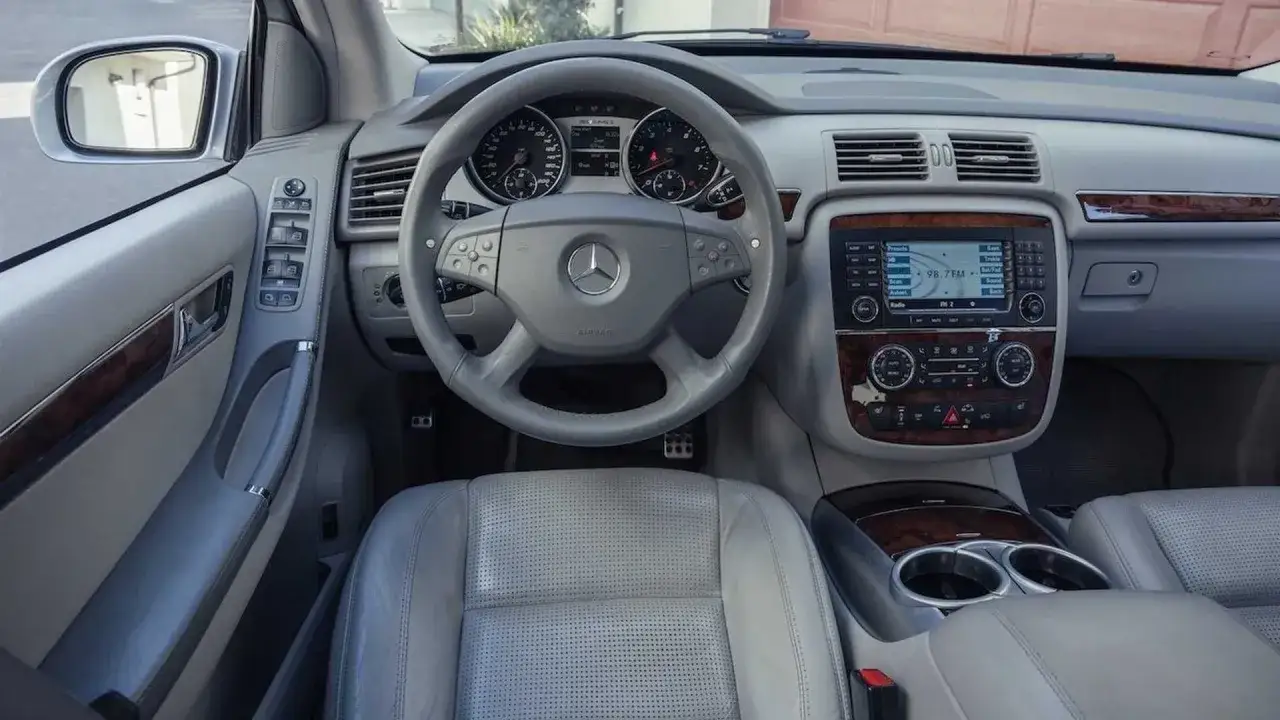 Wnętrze Mercedesa R-klasy z szarą, perforowaną skórą i drewnianymi wstawkami. Kierownica z logo gwiazdy, panel radia i nawigacji. Idealny dla fanów r63.