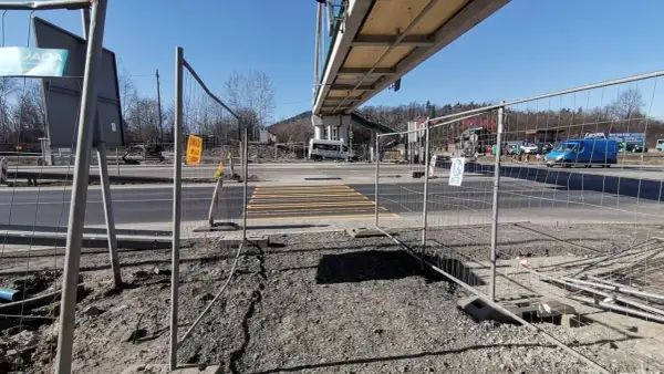 Przejście dla pieszych w budowie, ogrodzone siatką. W tle wiadukt i ruch uliczny. Kmy rejestracja.