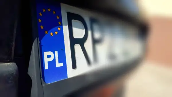 Zbliżenie na polską tablicę rejestracyjną z symbolem UE. Litery "PL" i fragment numeru rejestracyjnego są wyraźne.
