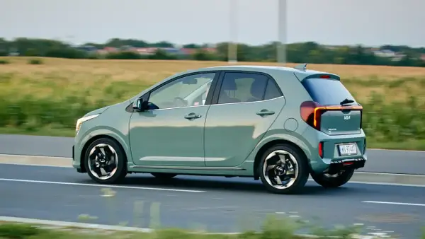 Zielony Kia Picanto w ruchu drogowym, widok z boku, z polem w tle.