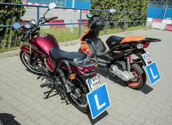 Dwa motorowery z tablicami "L" na parkingu.