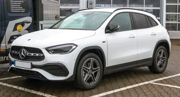 Biały Mercedes GLA, kompaktowy SUV, zaparkowany na mokrym parkingu. Jego wymiary idealnie pasują do miejskiej dżungli.