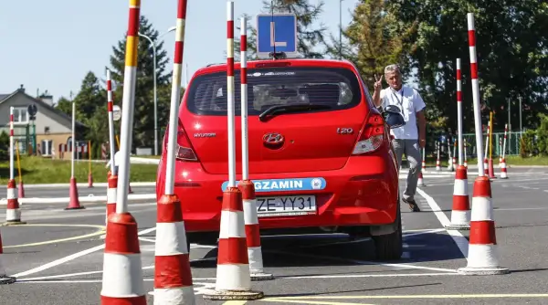 Czerwony Hyundai na placu manewrowym, gotowy do egzaminu na prawo jazdy B. Instruktor pokazuje znak zwycięstwa.