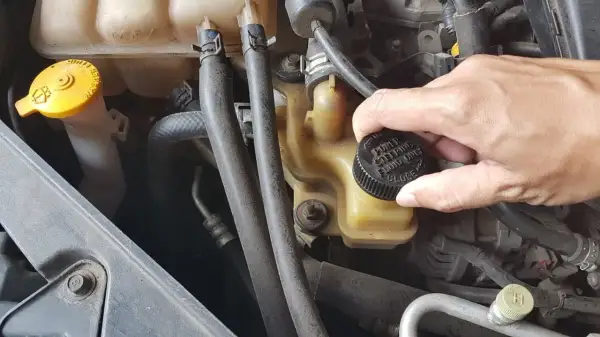 Dłoń odkręca korek zbiorniczka z napisem "POWER STEERING FLUID ONLY". Tu wlejesz płyn do wspomagania kierownicy.
