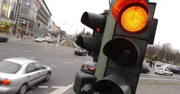 Pomarańczowe światło na sygnalizatorze drogowym. Ruch uliczny w mieście, samochody czekają na zmianę świateł.