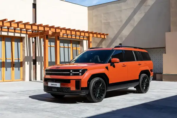Pomarańczowy, luksusowy SUV Santa Fe stoi przed nowoczesnym budynkiem z drewnianą pergolą.