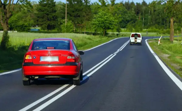 Czerwony Opel próbuje wyprzedzanie na podwójnej ciągłej, mandat murowany. Biały bus jedzie z przodu.