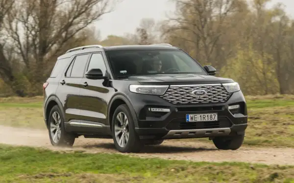 Czarny Ford Explorer 4x4 pokonuje piaszczystą drogę wśród jesiennej przyrody.