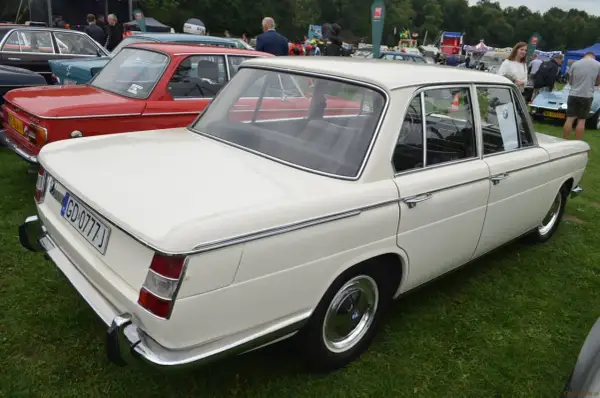 Białe BMW E10 z lat 70. prezentuje się elegancko na zielonej trawie, obok czerwonego klasyka.