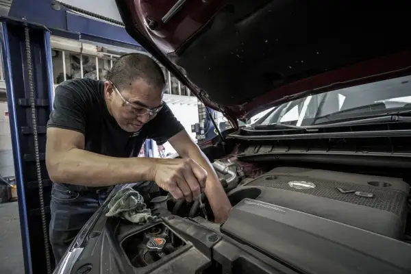 Mechanik w okularach ochronnych pracuje przy silniku. Zastanawiasz się, ile kosztuje wymiana oleju w skrzyni biegów?